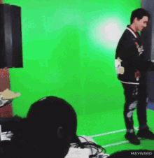 a man is standing in front of a green screen with mayward written on the bottom right