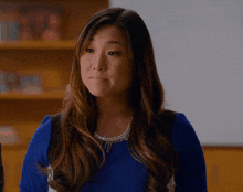 a woman wearing a blue sweater and a necklace is making a funny face