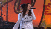 a woman singing into a microphone while wearing a shirt that says " хуй " on it