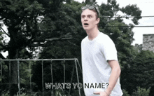 a young man in a white shirt is standing in front of a playground and asking what 's your name .