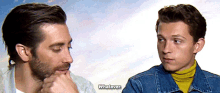 a man in a denim jacket is talking to another man in a turtleneck .