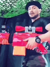a man wearing a hat and a watch is holding a red toy gun .