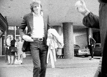 a man in a suit is walking down a street holding a jacket .
