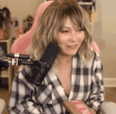 a woman in a plaid shirt is sitting in front of a microphone in a pink chair .