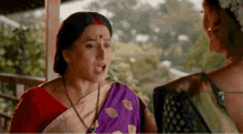a woman in a purple sari is talking to another woman in a red shirt .