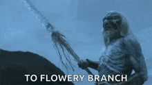 a skeleton with long hair and a beard is holding a stick in his hand and says `` to flowery branch '' .