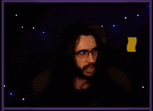 a man with long hair and glasses is sitting in a chair in front of a computer screen .