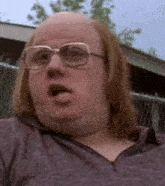 a close up of a bald man wearing glasses and a purple shirt .