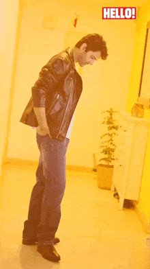 a man in a leather jacket is standing in front of a yellow wall with a hello sign above him