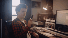 a man in a plaid shirt is sitting at a desk with a keyboard