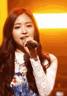 a woman singing into a microphone wearing a white lace top