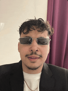 a man wearing sunglasses and a suit is looking at the camera