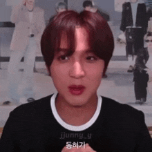 a young man with red hair is making a funny face in front of a wall with pictures of people .