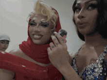 two drag queens are standing next to each other and one has a tattoo on her ring finger