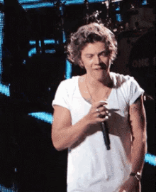 a man in a white shirt is singing into a microphone in front of a one direction shirt