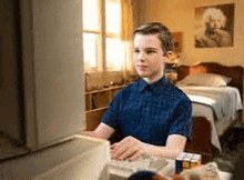 a young boy is sitting at a table in front of a computer in a bedroom .