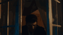a man is sitting in a dark room looking out of a window .
