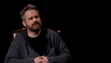 a man with a beard is sitting in a chair with the name jay bauman former baby above him