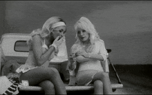 two women are sitting in the back of a truck one is smoking a cigarette