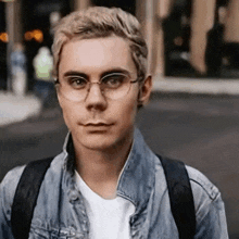 a young man wearing glasses and a denim jacket with a backpack
