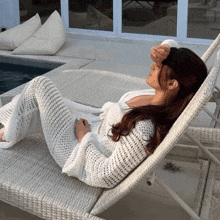 a woman in a white sweater is laying on a lounge chair by a pool