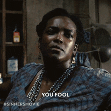 a woman wearing a necklace and earrings says you fool