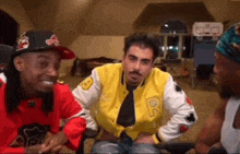 a group of men are sitting next to each other in a room . one of the men is wearing a yellow jacket .