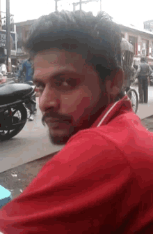 a man in a red shirt looks over his shoulder at the camera
