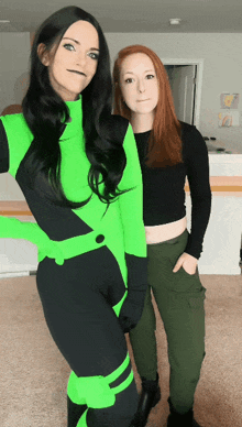 a woman in a green costume stands next to another woman in a black crop top