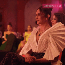 a woman in a white dress is sitting in front of a pinkvilla sign