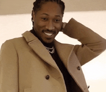 a man wearing a tan coat is smiling with his hand on his head