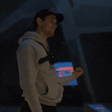 a man wearing a hat with the word supreme on it stands in front of a monitor
