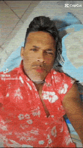 a man in a red hawaiian shirt is laying on a bed and looking at the camera .