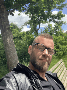 a man with glasses sits on a park bench