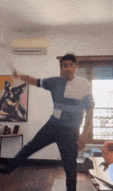 a man is dancing in a living room with a painting of a dog on the wall behind him