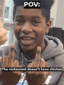 a young boy is giving the middle finger to a restaurant that does not have chicken .