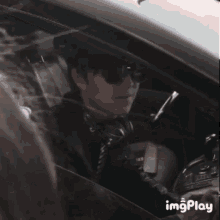a man wearing sunglasses is driving a car and looking out the window .