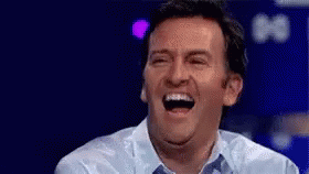 a man in a blue shirt is laughing with his eyes closed and his mouth open .