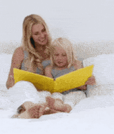 a woman sits on a bed reading a book to her daughter