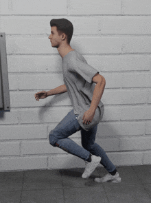 a man in a grey shirt and jeans is running against a brick wall