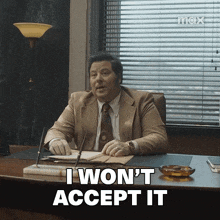 a man in a suit and tie is sitting at a desk and says i won 't accept it