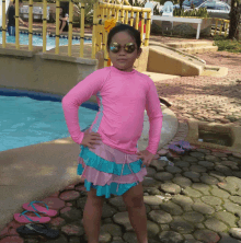 a little girl wearing sunglasses and a pink shirt is standing in front of a pool