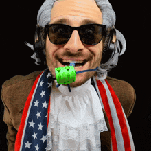 a man wearing a wig and sunglasses has a green object in his mouth that says ' a ' on it