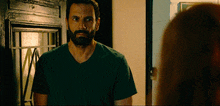 a man with a beard in a green shirt stands in front of a door