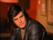 a man in a black leather jacket is sitting in front of a red wall