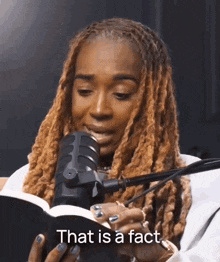 a woman with dreadlocks is reading a book in front of a microphone and says that is a fact .