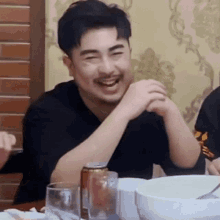 a man is laughing while sitting at a table with a can of soda and a glass of water