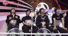 a group of young men are sitting in front of a stage that says boys planet on it