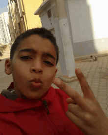 a young boy in a red jacket is making a face and giving the middle finger