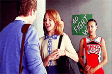 two cheerleaders are standing in front of a green sign that says go fight